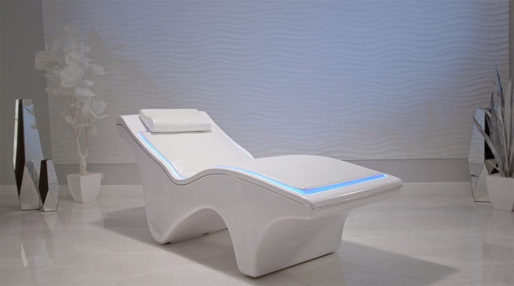 The PureWave VEMI Bed, a sculpted white lounger with blue edge lighting