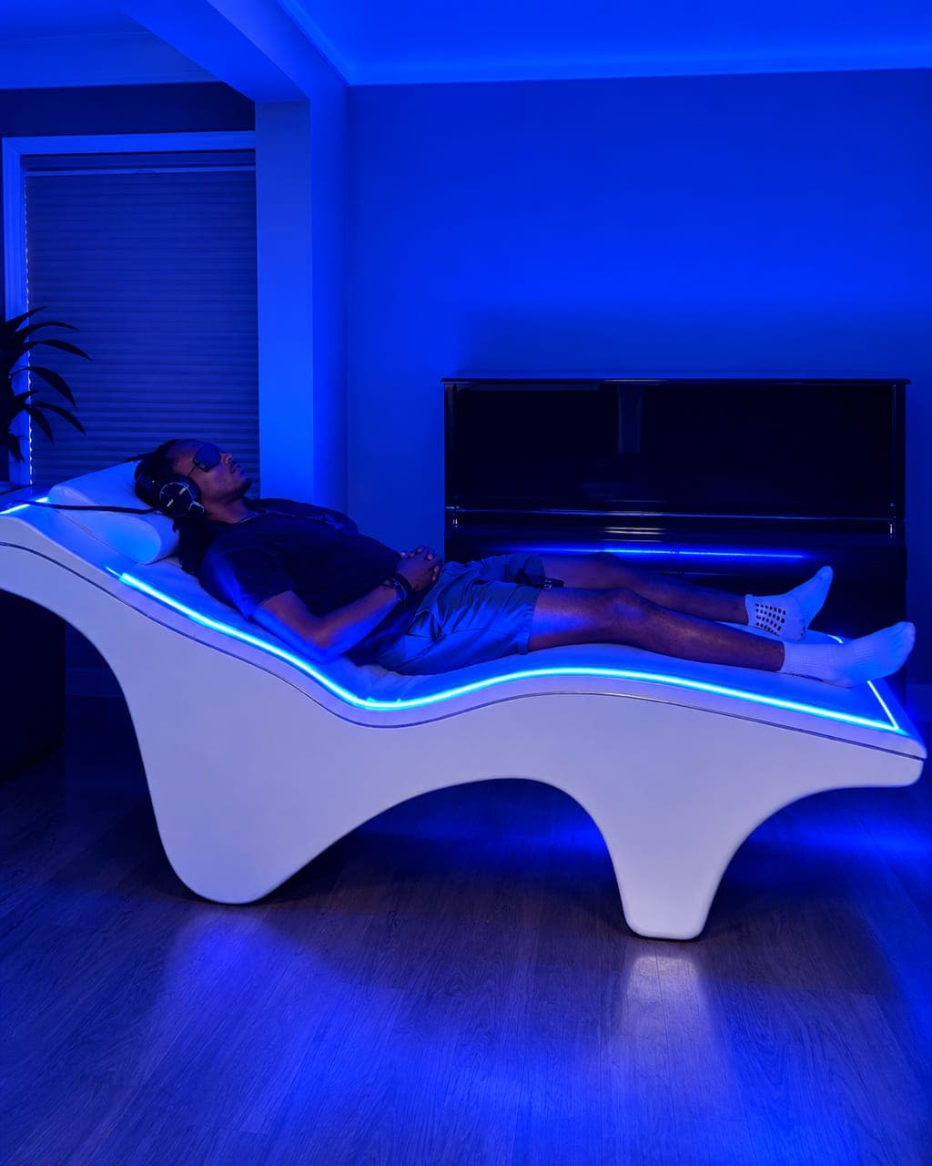 Person resting on the VEMI Bed wearing headphones and an eye mask during a vibroacoustic relaxation session